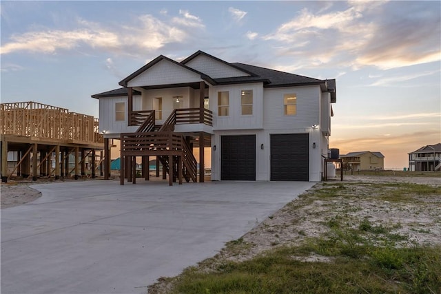 coastal inspired home featuring concrete driveway, stairway, roof with shingles, and an attached garage