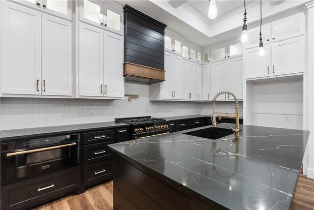 kitchen with light wood-style flooring, ornamental molding, white cabinetry, a sink, and a tray ceiling