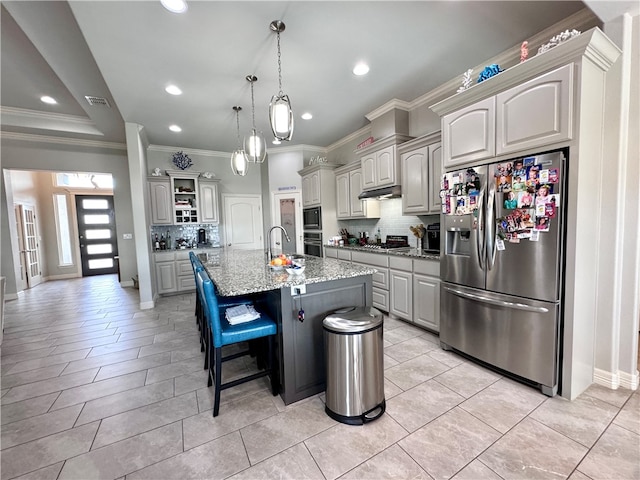 kitchen with a center island with sink, a breakfast bar, appliances with stainless steel finishes, light stone countertops, and backsplash