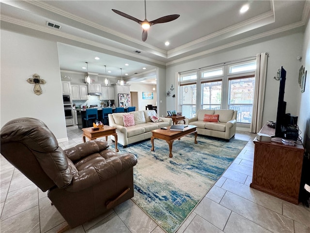 living room with ceiling fan, a tray ceiling, light tile patterned floors, and ornamental molding