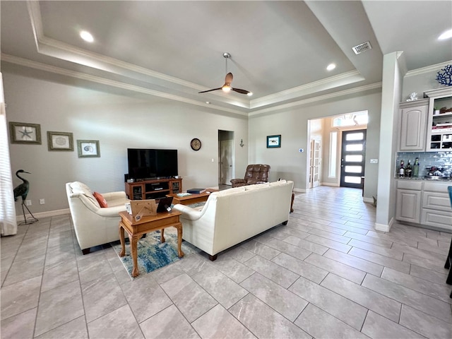 living room with a tray ceiling, ceiling fan, and crown molding