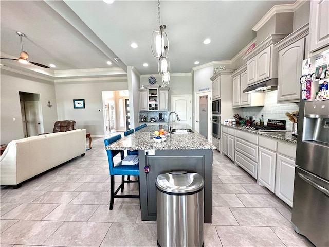 kitchen with a center island with sink, sink, light stone counters, appliances with stainless steel finishes, and crown molding