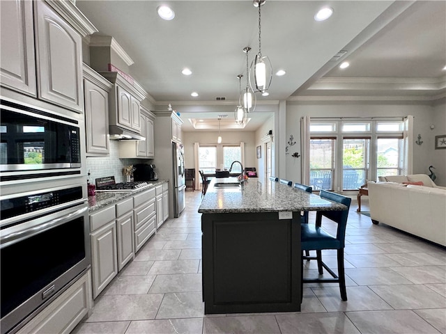 kitchen featuring sink, appliances with stainless steel finishes, light stone countertops, a kitchen bar, and an island with sink