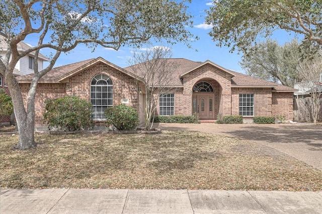 ranch-style house featuring roof with shingles, a front lawn, french doors, and brick siding