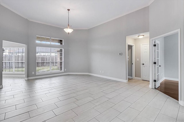 unfurnished room featuring ornamental molding, a towering ceiling, and baseboards