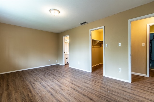 unfurnished bedroom featuring hardwood / wood-style floors, ensuite bath, a spacious closet, and a closet