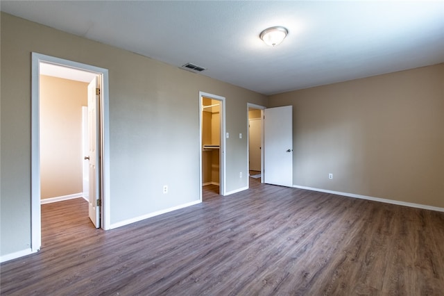 unfurnished bedroom with dark wood-type flooring, a closet, and a walk in closet