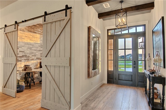 entrance foyer with beamed ceiling, a chandelier, a barn door, and light hardwood / wood-style flooring