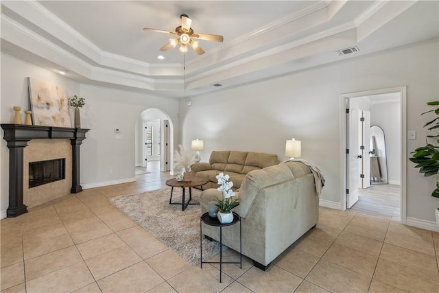living area featuring visible vents, a ceiling fan, a raised ceiling, arched walkways, and light tile patterned floors