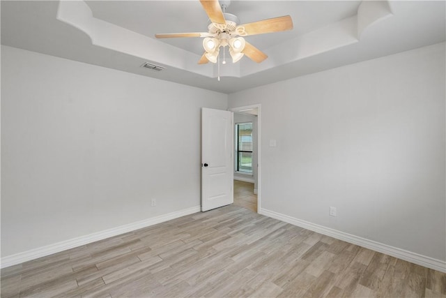 unfurnished room with a raised ceiling, baseboards, light wood-style flooring, and visible vents