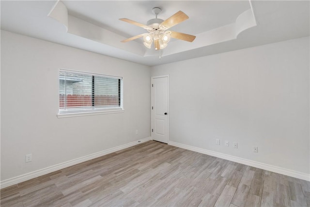 spare room with a raised ceiling, ceiling fan, baseboards, and light wood finished floors