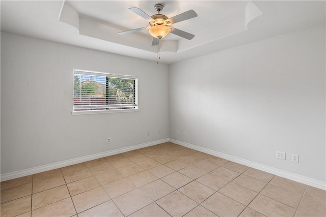 empty room featuring light tile patterned flooring, ceiling fan, baseboards, and a raised ceiling