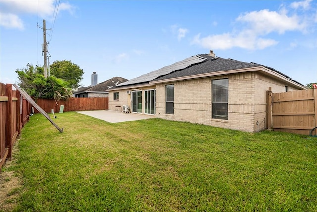 back of property featuring a lawn, a patio area, brick siding, a fenced backyard, and roof mounted solar panels