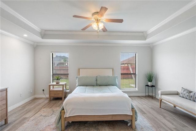 bedroom featuring multiple windows, ornamental molding, a tray ceiling, and light wood finished floors