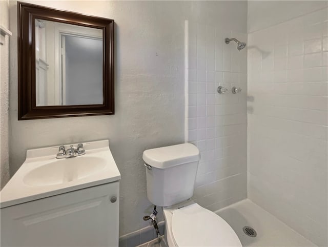 bathroom featuring a tile shower, vanity, and toilet