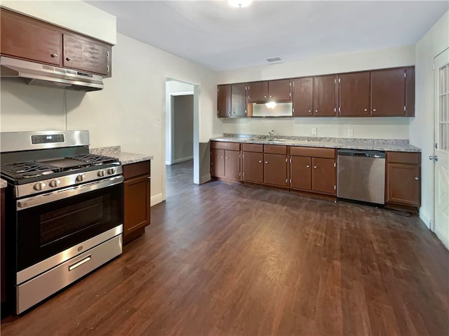 kitchen with stainless steel appliances, dark wood-type flooring, dark brown cabinetry, sink, and light stone countertops