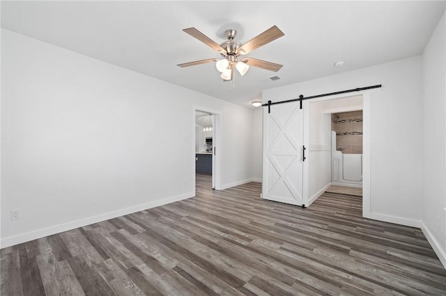 unfurnished bedroom with ceiling fan, a barn door, dark hardwood / wood-style floors, and a closet