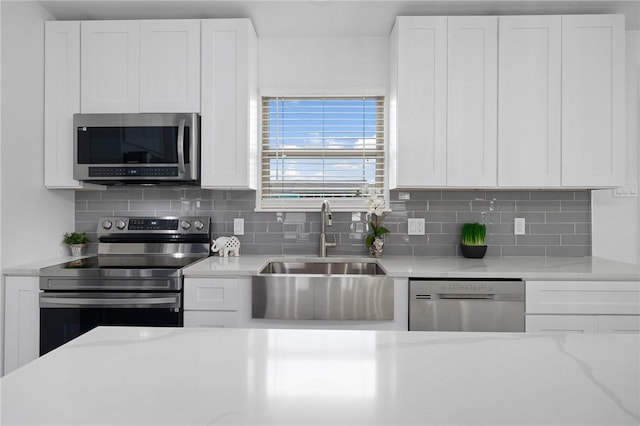 kitchen featuring sink, decorative backsplash, light stone countertops, white cabinetry, and stainless steel appliances