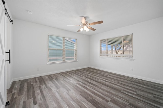 empty room featuring a barn door, dark hardwood / wood-style floors, a wealth of natural light, and ceiling fan