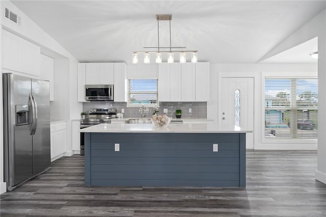 kitchen featuring white cabinets, hanging light fixtures, appliances with stainless steel finishes, and vaulted ceiling