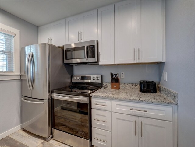 kitchen featuring white cabinets, light hardwood / wood-style floors, light stone counters, and appliances with stainless steel finishes