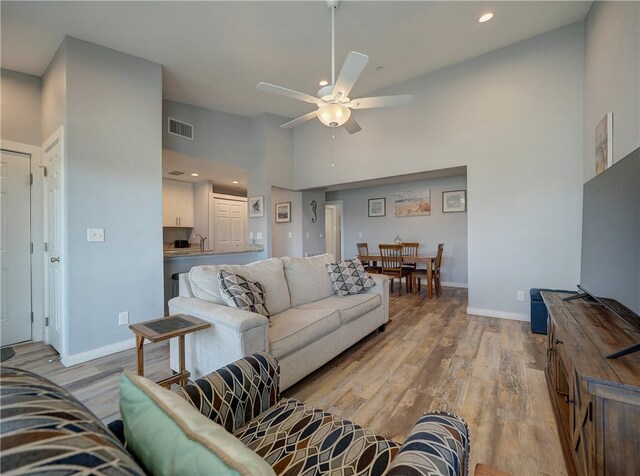 living room with light hardwood / wood-style flooring, ceiling fan, a high ceiling, and sink