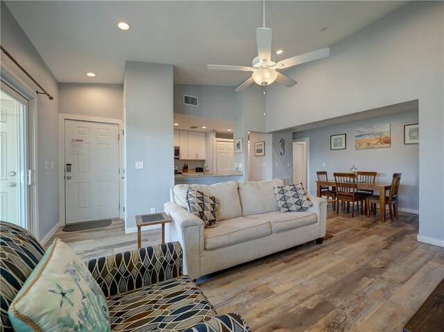 living room featuring light wood-type flooring, ceiling fan, and high vaulted ceiling