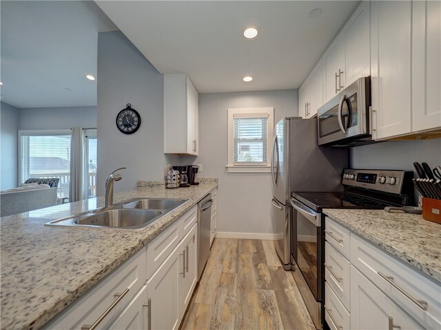 kitchen with sink, appliances with stainless steel finishes, light stone countertops, light hardwood / wood-style flooring, and white cabinets