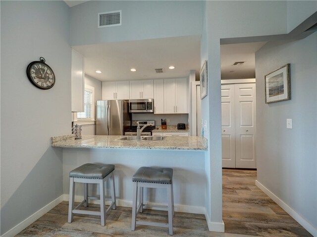 kitchen featuring stainless steel appliances, white cabinetry, light stone countertops, sink, and light hardwood / wood-style floors