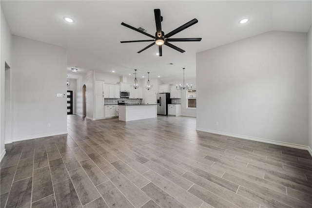 unfurnished living room with hardwood / wood-style floors, ceiling fan with notable chandelier, and vaulted ceiling