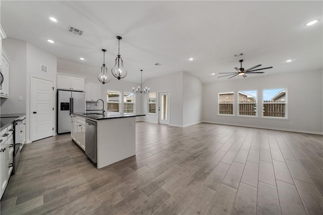 kitchen with white cabinetry, hanging light fixtures, stainless steel appliances, a kitchen island with sink, and ceiling fan with notable chandelier