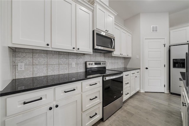 kitchen with decorative backsplash, appliances with stainless steel finishes, white cabinetry, and dark stone countertops