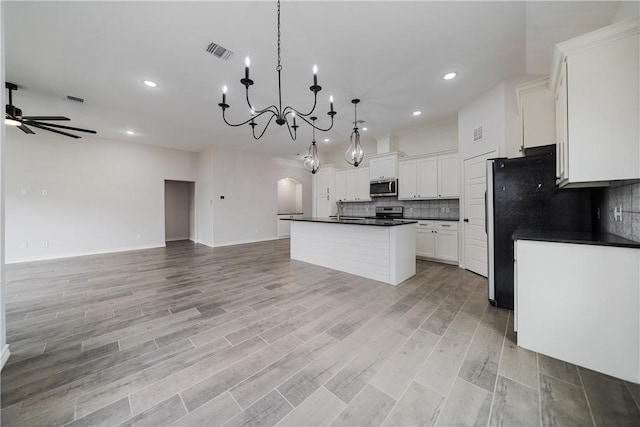 kitchen with ceiling fan with notable chandelier, hanging light fixtures, an island with sink, appliances with stainless steel finishes, and white cabinetry