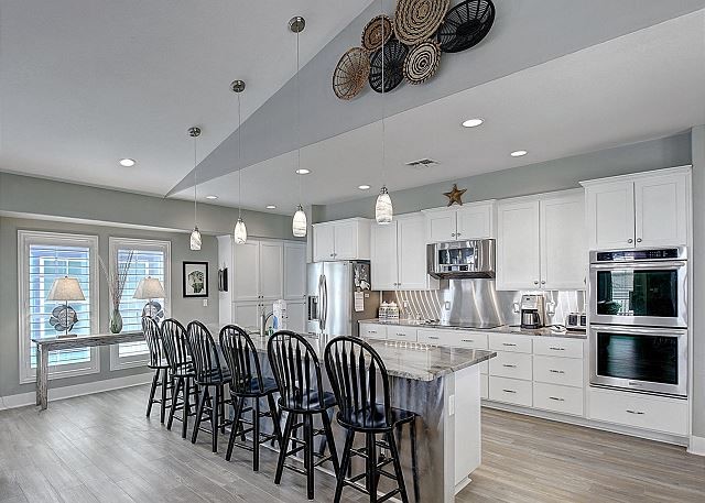 kitchen featuring appliances with stainless steel finishes, white cabinetry, an island with sink, hanging light fixtures, and vaulted ceiling