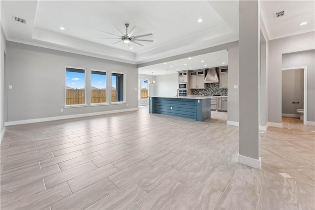 unfurnished living room featuring ceiling fan, crown molding, and a tray ceiling