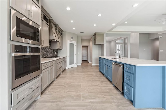 kitchen with decorative backsplash, stainless steel appliances, sink, blue cabinetry, and an island with sink