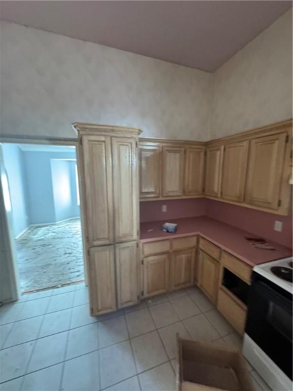 kitchen with light countertops, light tile patterned floors, electric range oven, and light brown cabinetry