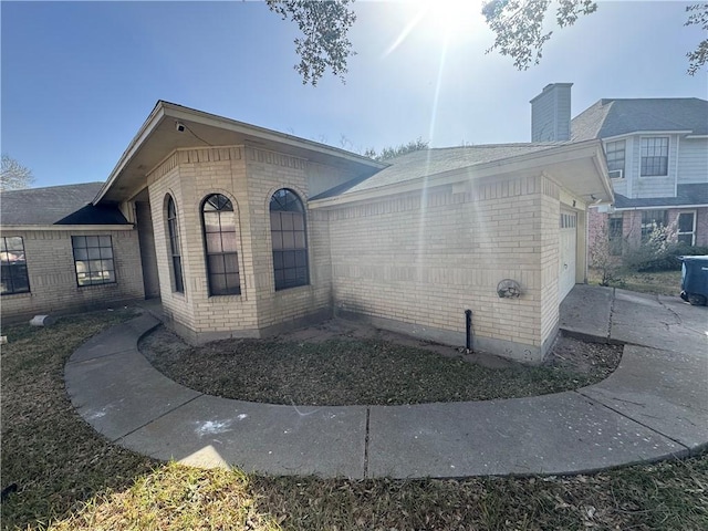 view of property exterior with brick siding, an attached garage, and driveway