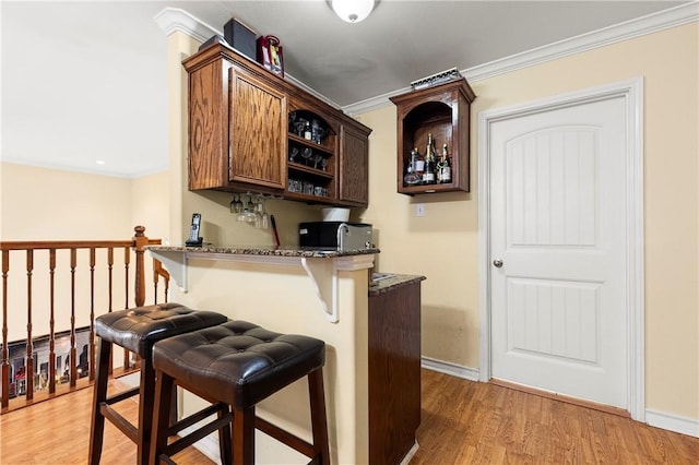 kitchen with crown molding, light hardwood / wood-style flooring, dark stone countertops, kitchen peninsula, and a breakfast bar area