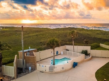 pool at dusk with a water view, a patio, and a view of the beach