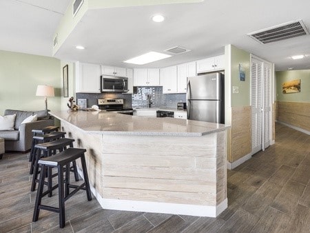 kitchen with white cabinetry, dark hardwood / wood-style flooring, kitchen peninsula, a kitchen bar, and appliances with stainless steel finishes