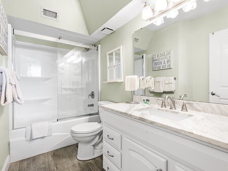 full bathroom with vanity, shower / bath combination with glass door, lofted ceiling, hardwood / wood-style flooring, and toilet