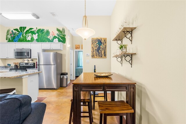 kitchen featuring white cabinetry, appliances with stainless steel finishes, pendant lighting, and light stone countertops