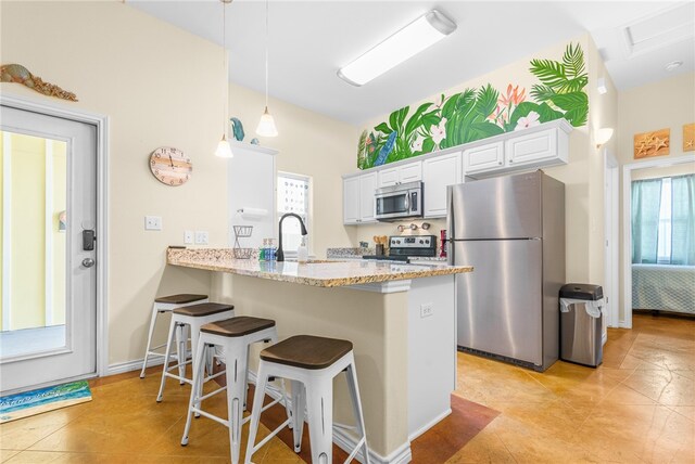 kitchen featuring stainless steel appliances, white cabinets, kitchen peninsula, light stone countertops, and pendant lighting