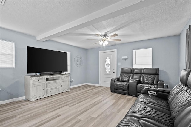 living room featuring ceiling fan, light hardwood / wood-style flooring, beamed ceiling, and a textured ceiling