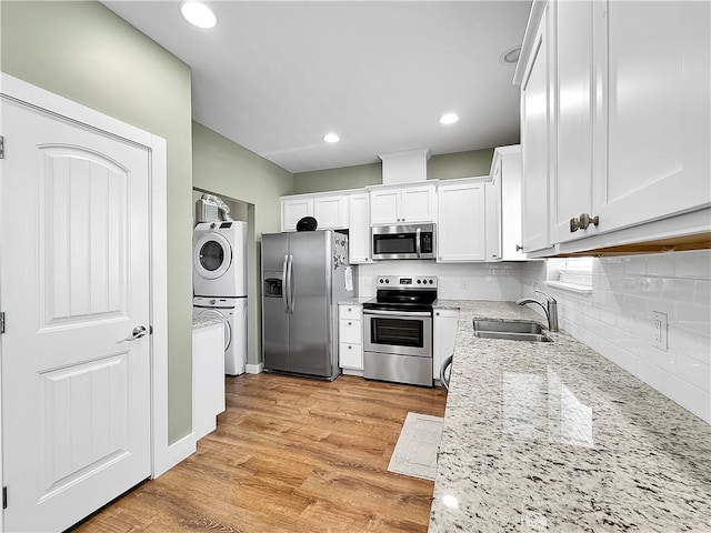 14307 Ridley Way, Corpus Christi, TX 78418 - kitchen with appliances with stainless steel finishes, a sink, stacked washing machine and dryer, light stone counters, and white cabinetry