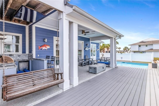 wooden terrace featuring fence, an outdoor kitchen, a fenced in pool, a patio area, and a ceiling fan