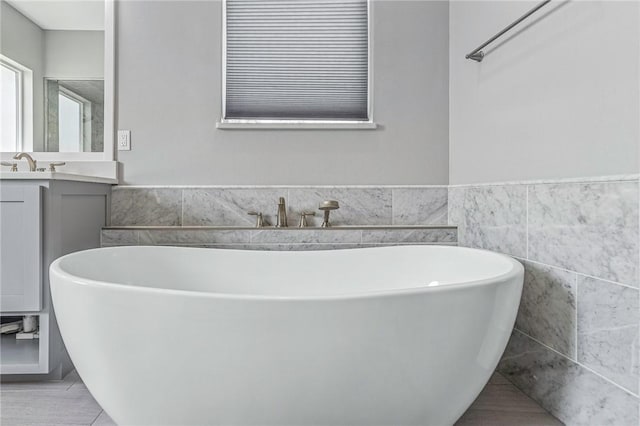 bathroom featuring tile walls, a freestanding bath, a wainscoted wall, and vanity