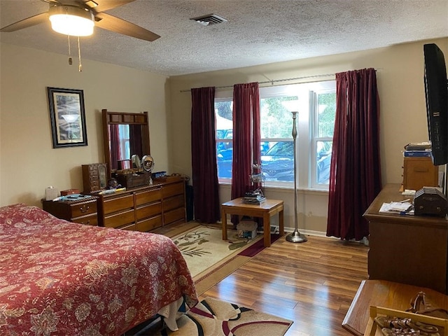 bedroom with ceiling fan, wood-type flooring, and a textured ceiling