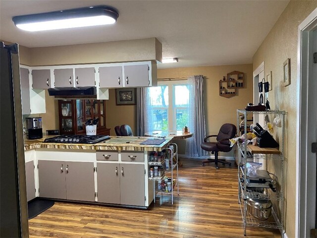 kitchen featuring stainless steel gas cooktop, extractor fan, kitchen peninsula, wood-type flooring, and white cabinets